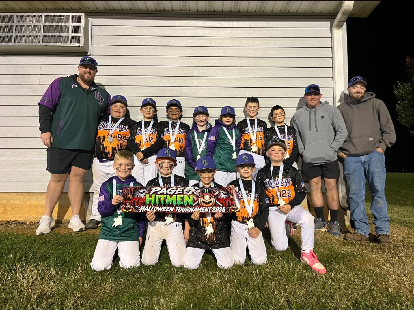 Dirtbags team in Halloween tournament jerseys holding a banner and medals at night